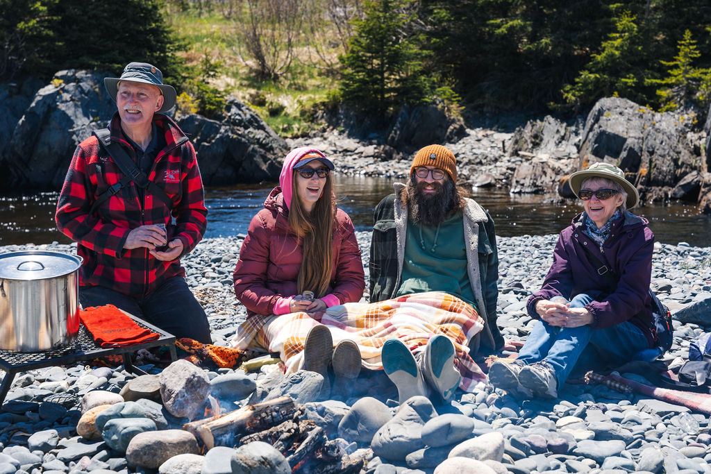 Family sitting around the fire smiling at a Wildera beach boil up in Mobile, Newfoundland